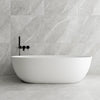 White freestanding bathtub against a grey onyx stone effect tiled wall with black faucet.