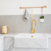 Modern kitchen with marble countertop, gold faucet, and white hexagonal mosaic tile backsplash.