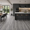 Grey wood-look plank flooring shown in a modern kitchen and dining room setting, with dark gray cabinets, a white island, and black pendant lights.