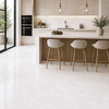 A bright, modern kitchen interior with glossy white onyx floor tiles, a central island, three light beige bar stools, and a clean backsplash. No people or animals are present.