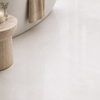 Large-format glossy white floor tiles in a modern bathroom setting, with a stone side table, a folded beige towel, and part of a bathtub visible.