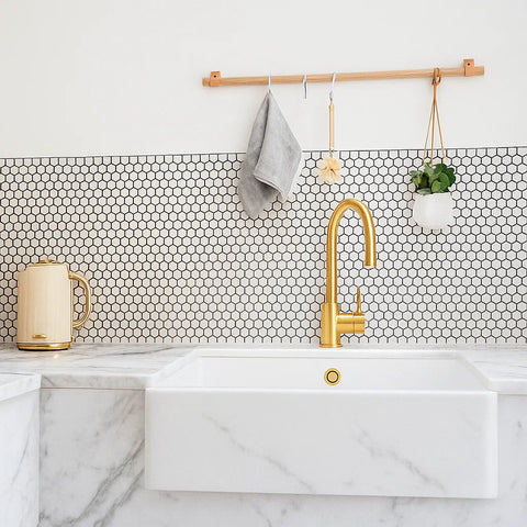 Modern kitchen with marble countertop, gold faucet, and white hexagonal mosaic tile backsplash.