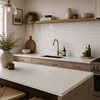 A modern kitchen interior with a white subway tile backsplash, light wood cabinetry, a white marble countertop, a brass faucet, and open shelving with decorative vases and plants.