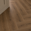 Brown wood-look porcelain flooring tiles arranged in a herringbone pattern, shown in a room setting with a light-colored baseboard visible on the left.