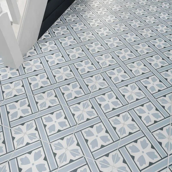 Mr Jones Pattern Light blue and white patterned ceramic floor tiles arranged in a geometric grid design, shown with a white chair leg in the top left corner.