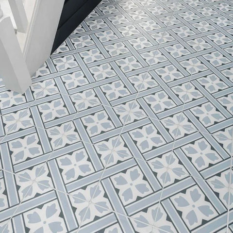 Mr Jones Pattern Light blue and white patterned ceramic floor tiles arranged in a geometric grid design, shown with a white chair leg in the top left corner.