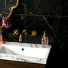 Bathroom sink with gold faucet and decorative bottles against a black marble wall.