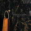 Gold towel ring with a brown towel on a black marble wall.