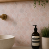 Bottle of Aesop product on a bathroom counter with hexagonal tiles and a plant in the background