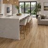 Light oak wood plank flooring shown in a modern kitchen and living room setting, featuring a white kitchen island with white bar stools and a light gray sofa.